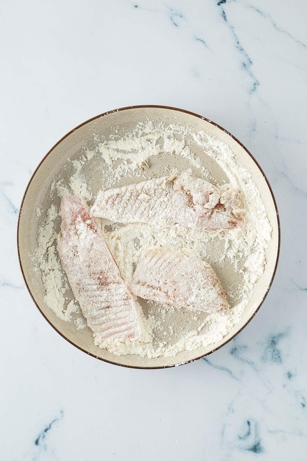 Fischfilets werden in einer Sch&uuml;ssel mit Mehl gewendet.