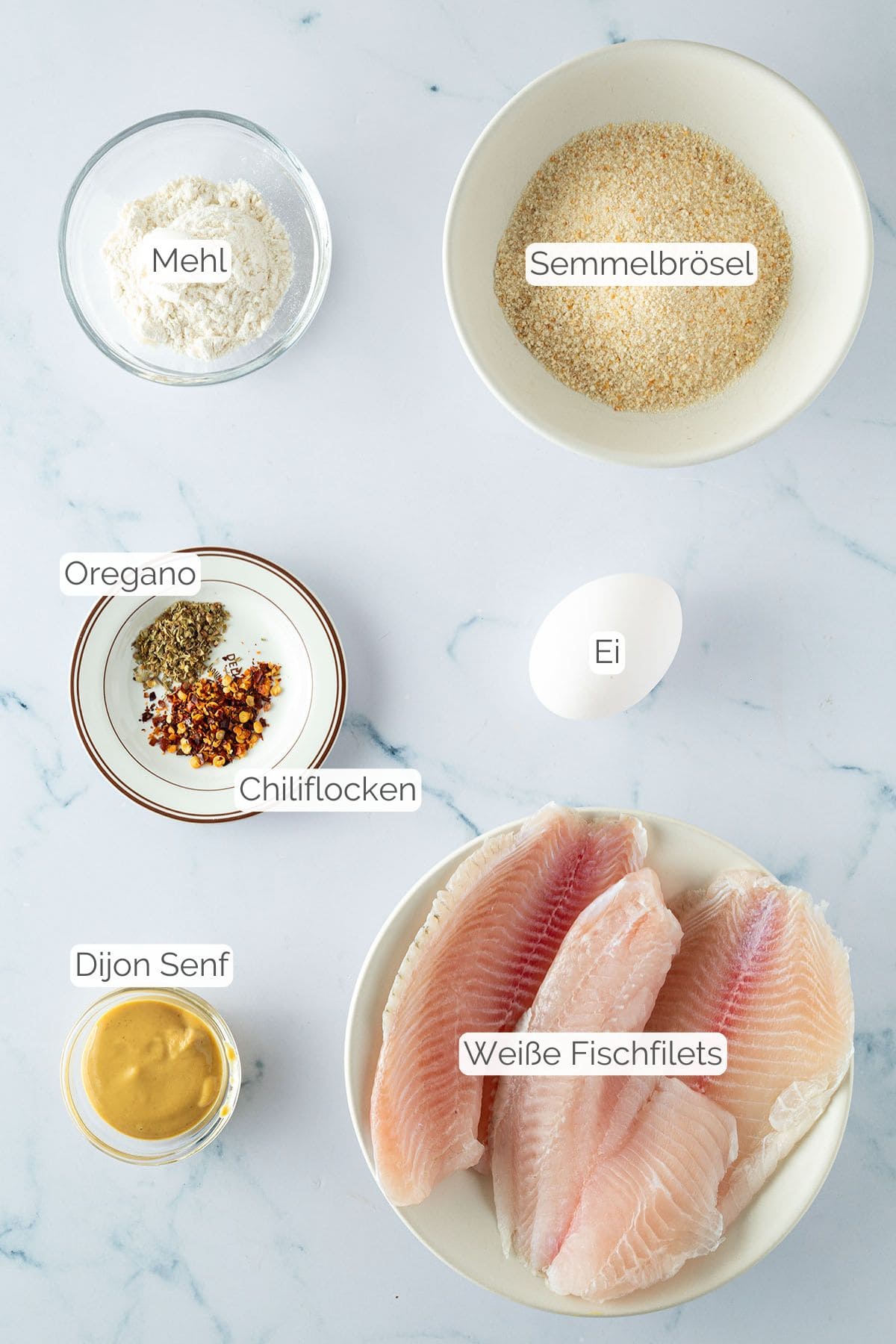Alle Zutaten mit jeweiligen Textbeschriftungen, die f&uuml;r panierten Fisch aus dem Airfryer ben&ouml;tigt werden.