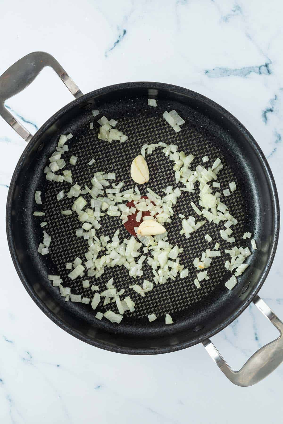 Fein gew&uuml;rfelte Schalotten und zwei ganze, gesch&auml;lte Knoblauchzehen werden in einer tiefen Pfanne anged&uuml;nstet.