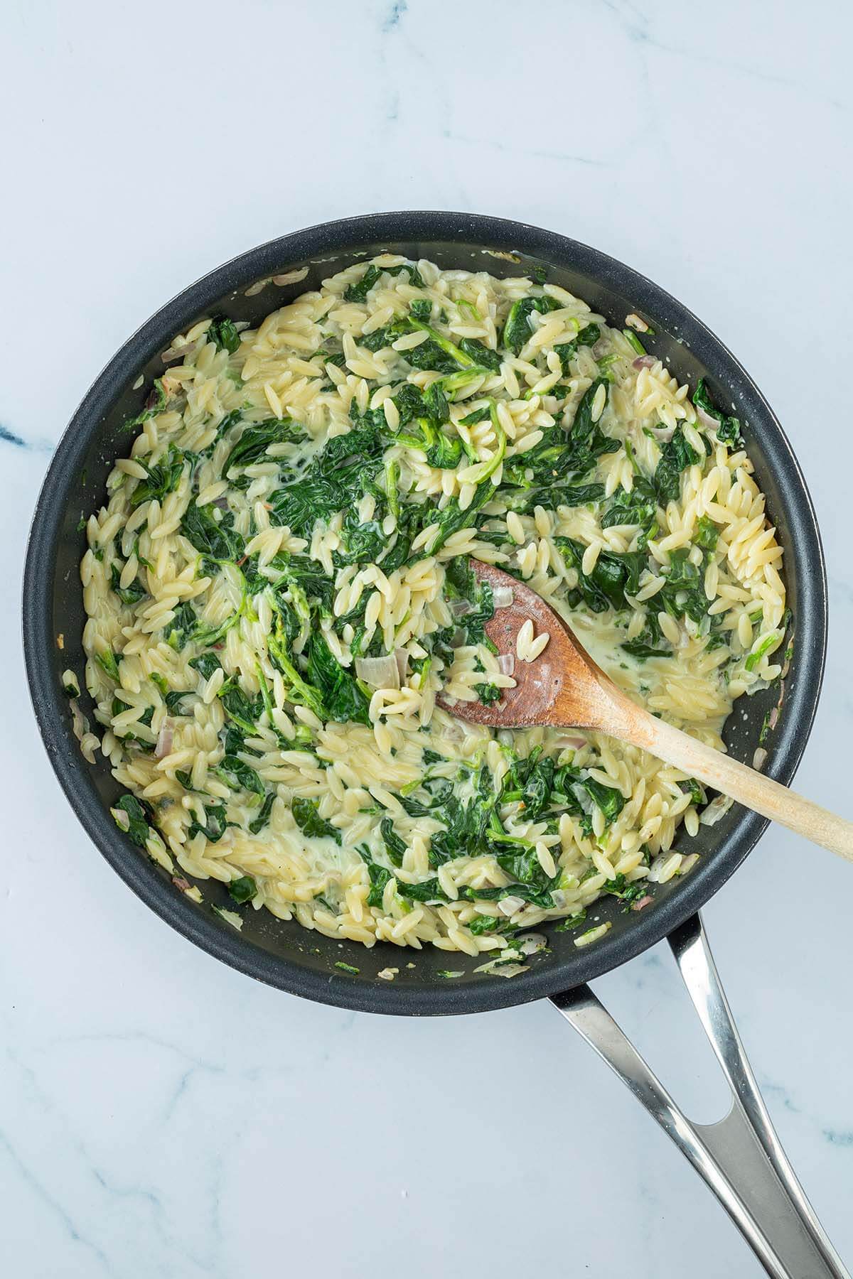 Vogelperspektive auf eine Pfanne mit kurzen Nudeln in einer cremigen Frischk&auml;se-Spinatsauce.