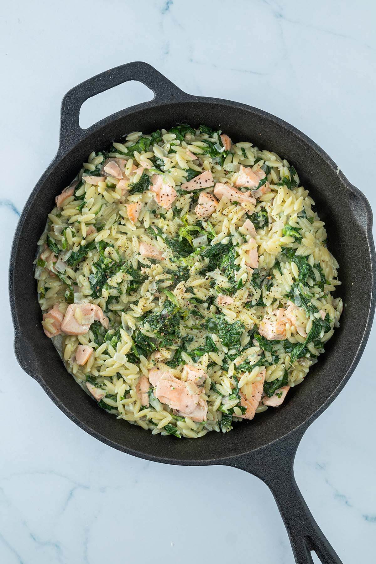 Fertige Lachs-Pasta mit Spinat in einer schwarzen Gusseisenpfanne.