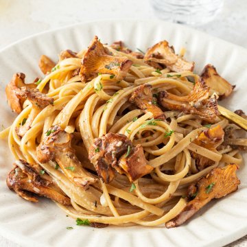 Ein Teller Pasta mit Pfifferlingen in einer cremigen Sauce und im Hintergrund ein Wasserglas.