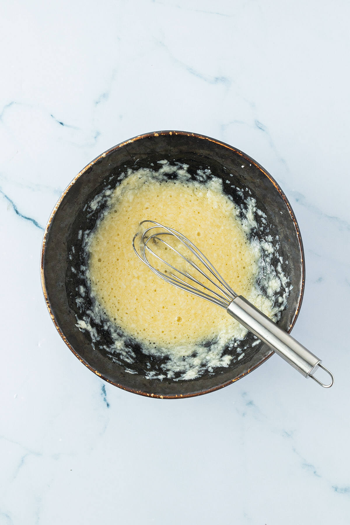 Verquirlte Eier-Parmesan-Mischung in einer Sch&uuml;ssel mit einem Mini-Schneebesen.