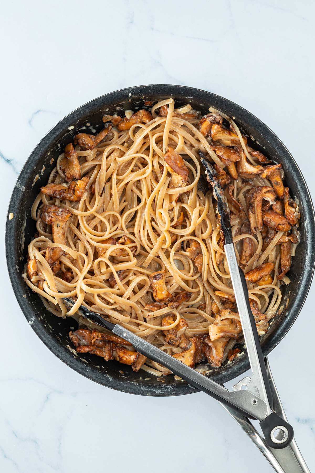 Cremige Pfifferlingspasta in einer Pfanne mit einer K&uuml;chenzange.