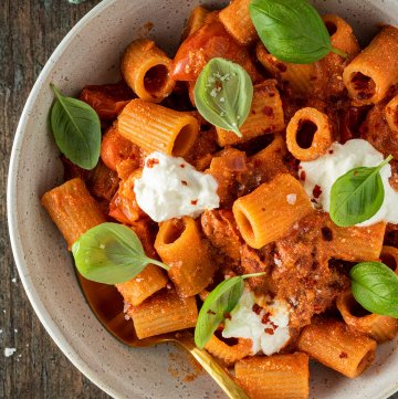 Nahaufnahme von einem Teller Rigatoni in einer cremigen Ricotta-Tomatenso&szlig;e, serviert mit frischem Basilikum und Ricotta.