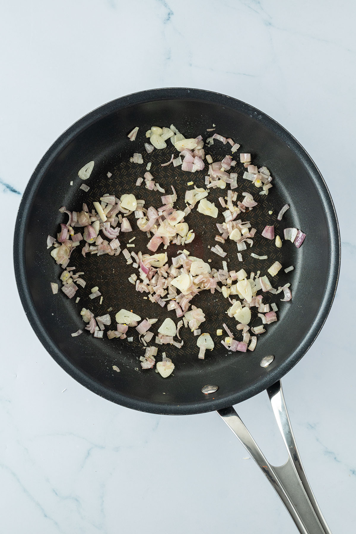 Schalotten und Knoblauch werden in einer Pfanne angebraten.