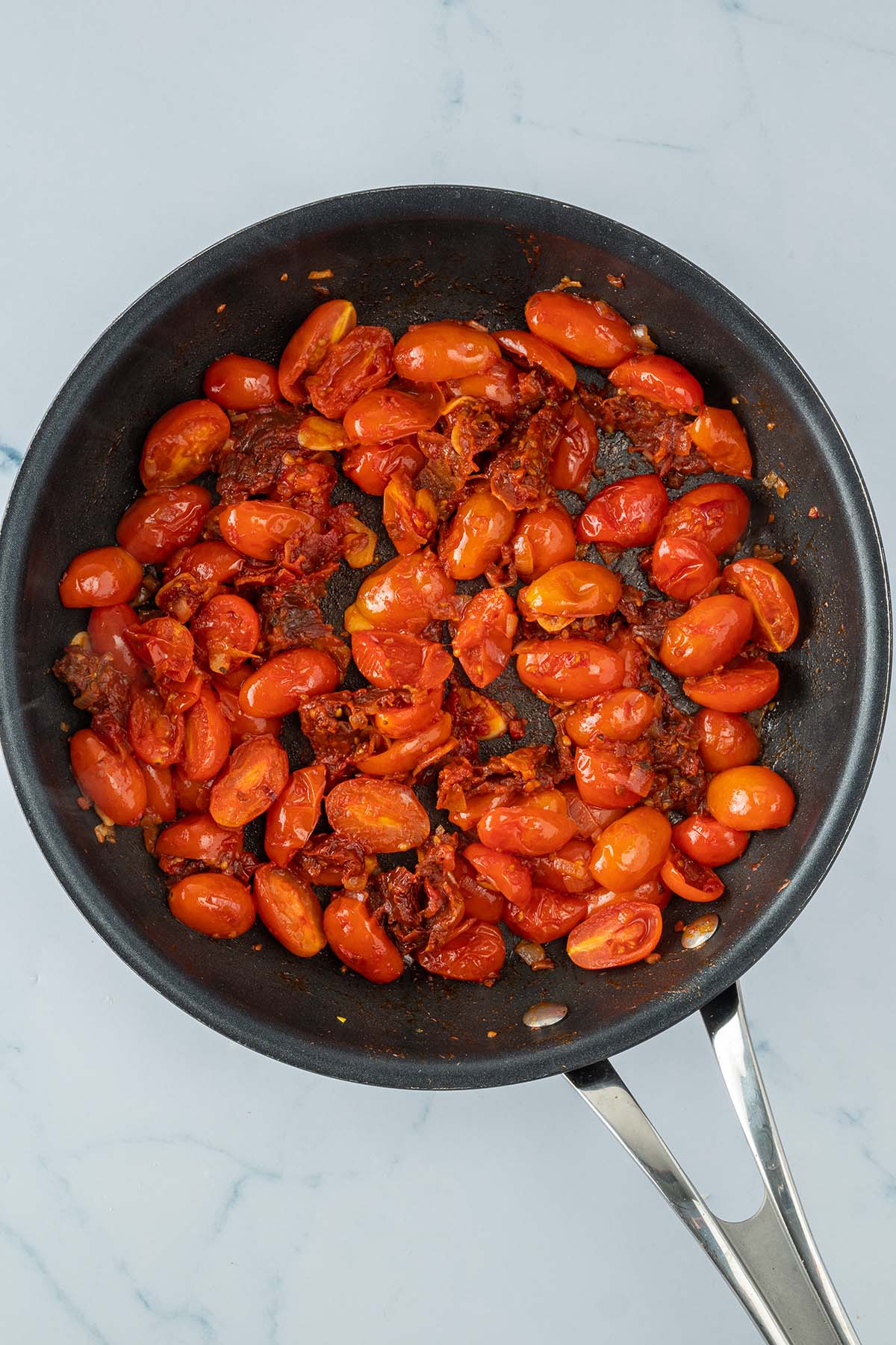 Angebratene Kirschtomaten in einer Pfanne mit getrockneten Tomaten, Tomatenmark und Zwiebeln.