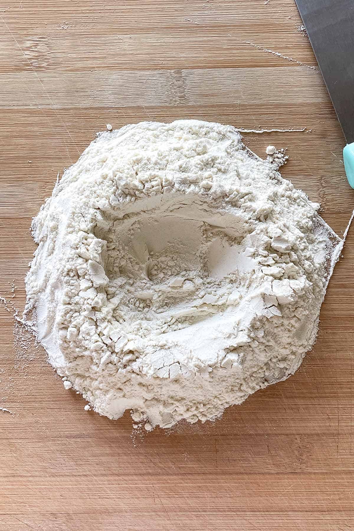 Mehl mit einer gro&szlig;en Mulde in der Mitte auf einer Holzarbeitsfl&auml;che.