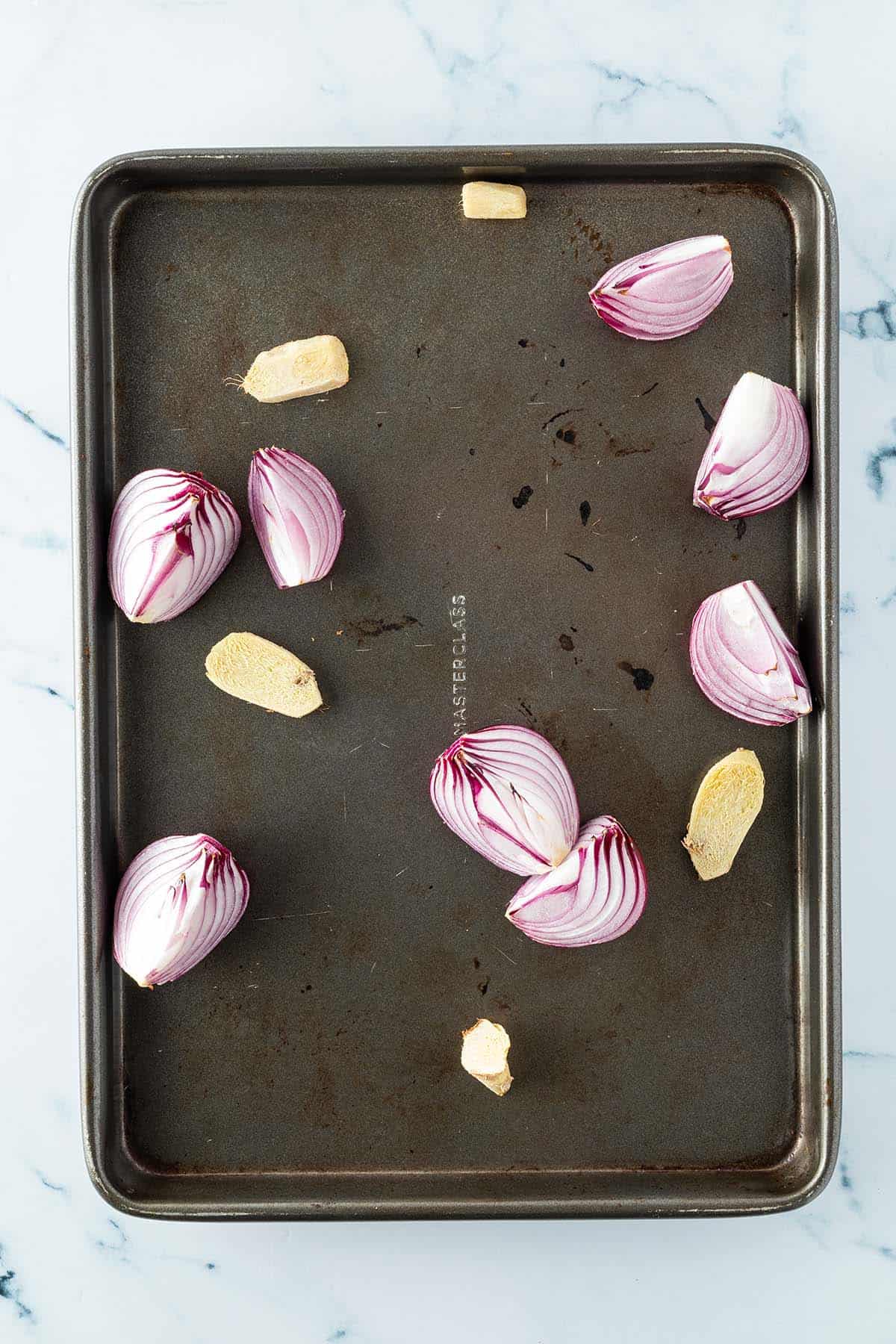 Im Ofen ger&ouml;stete Zwiebel- und Ingwerst&uuml;cke auf einem Backblech.