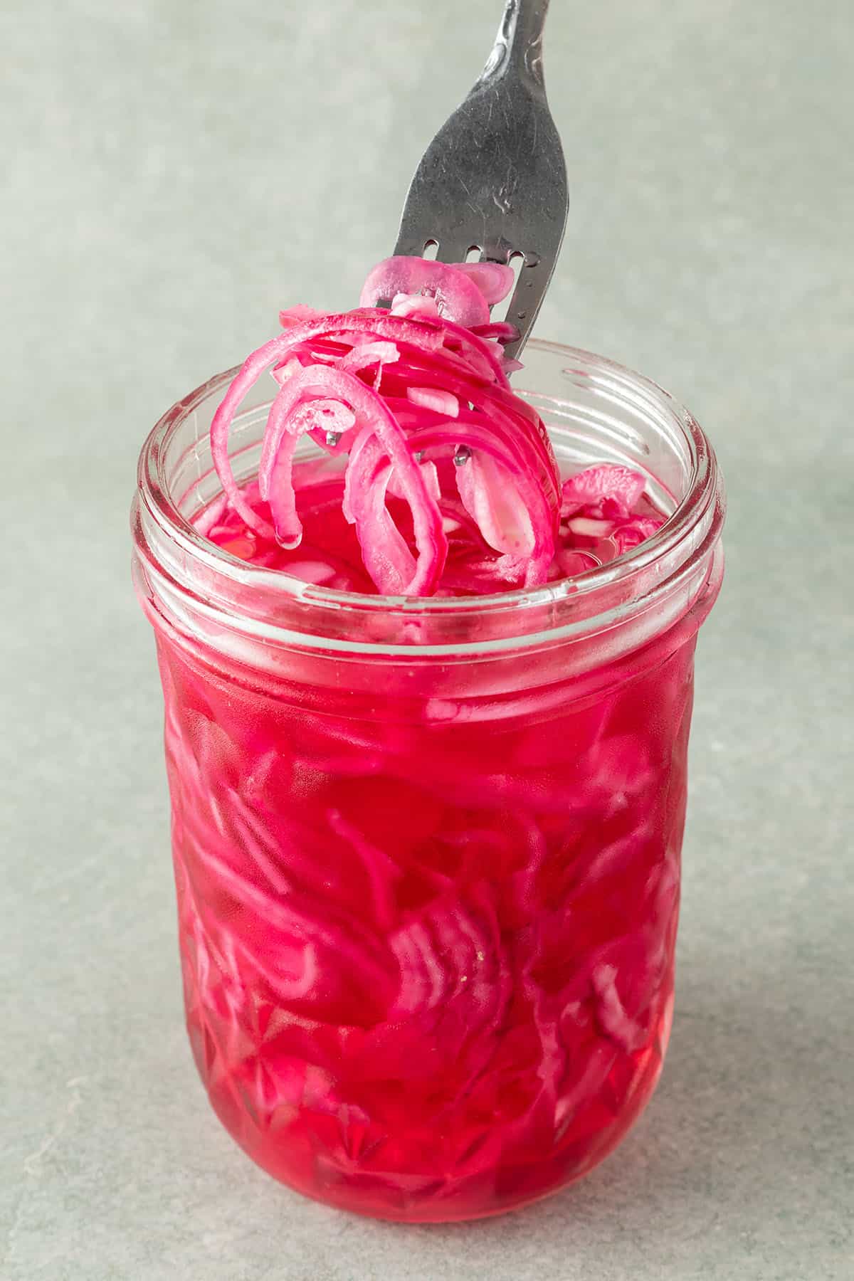 Ein Glas mit eingelegten Zwiebeln, wo eine Gabel ein paar Zwiebelringe rausholt.