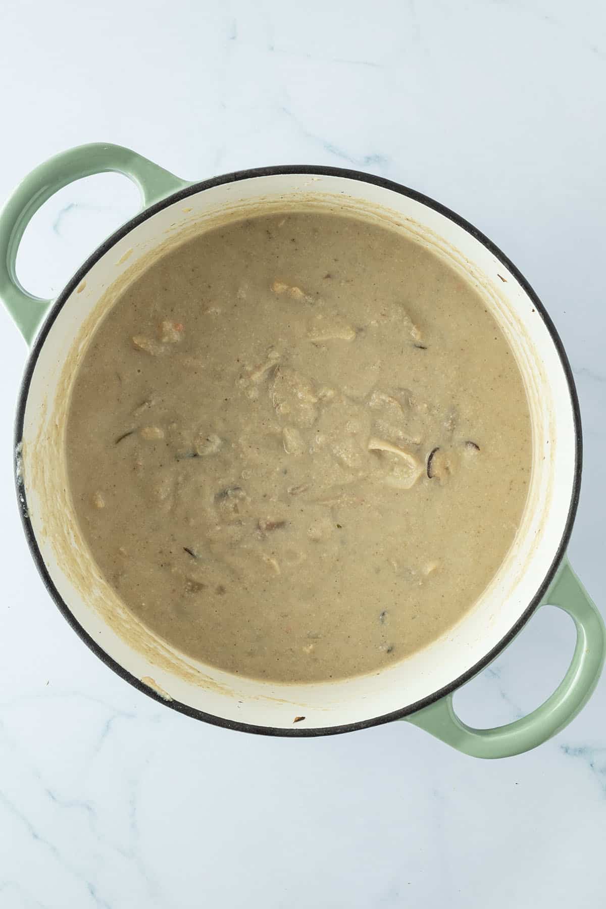 Cremige Pilzsuppe in einem Topf, bei der circa die H&auml;lfte der Pilze noch ganz sind.