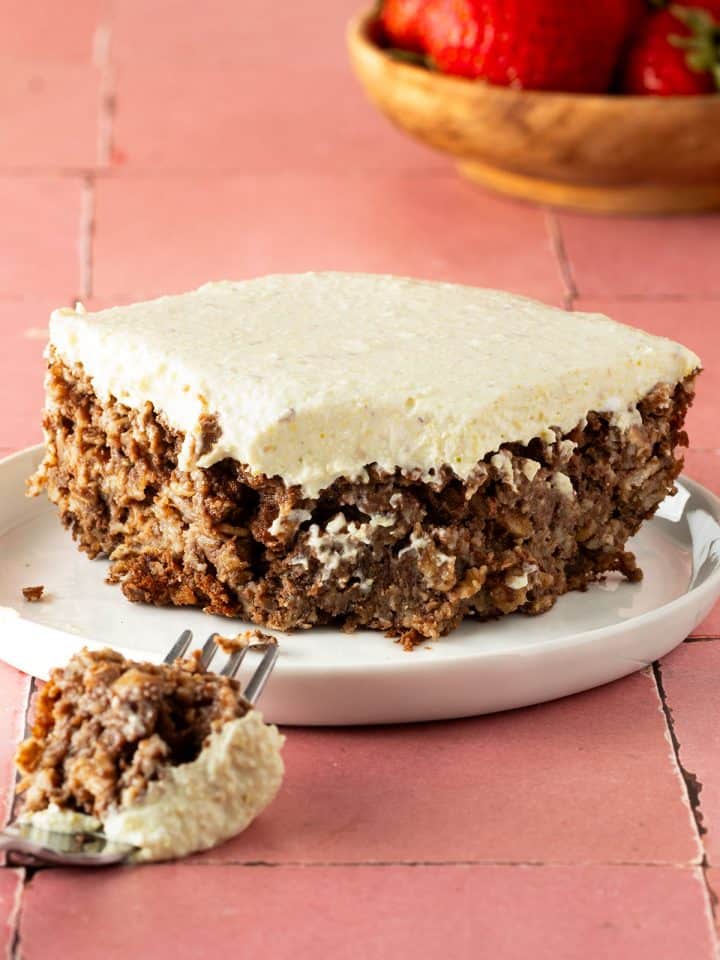 EIn St&uuml;ck Pistazien Baked Oatmeal auf einem Teller, ein St&uuml;ck davon auf einer Gabel liegt davor, eine Sch&uuml;ssel Erdbeeren im Hintergrund.