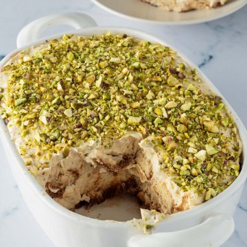 Pistazien Tiramisu in einer Auflaufform, ein Stück auf einem Teller im Hintergrund.