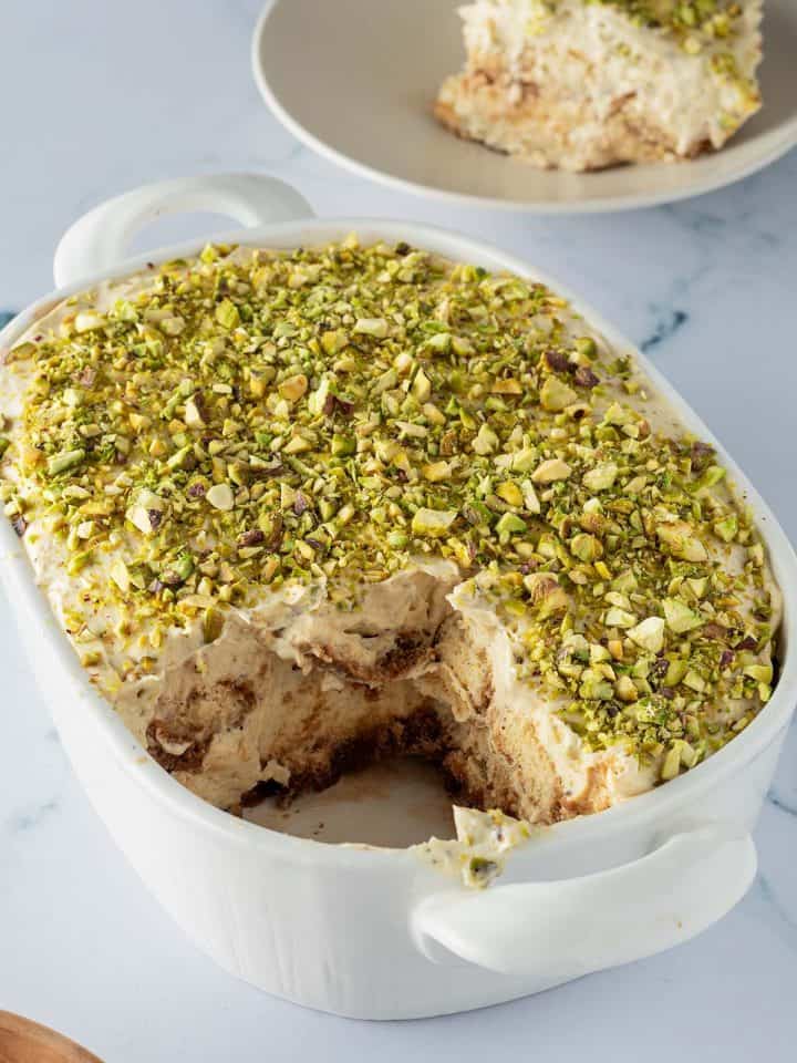 Pistazien Tiramisu in einer Auflaufform, ein St&uuml;ck auf einem Teller im Hintergrund.
