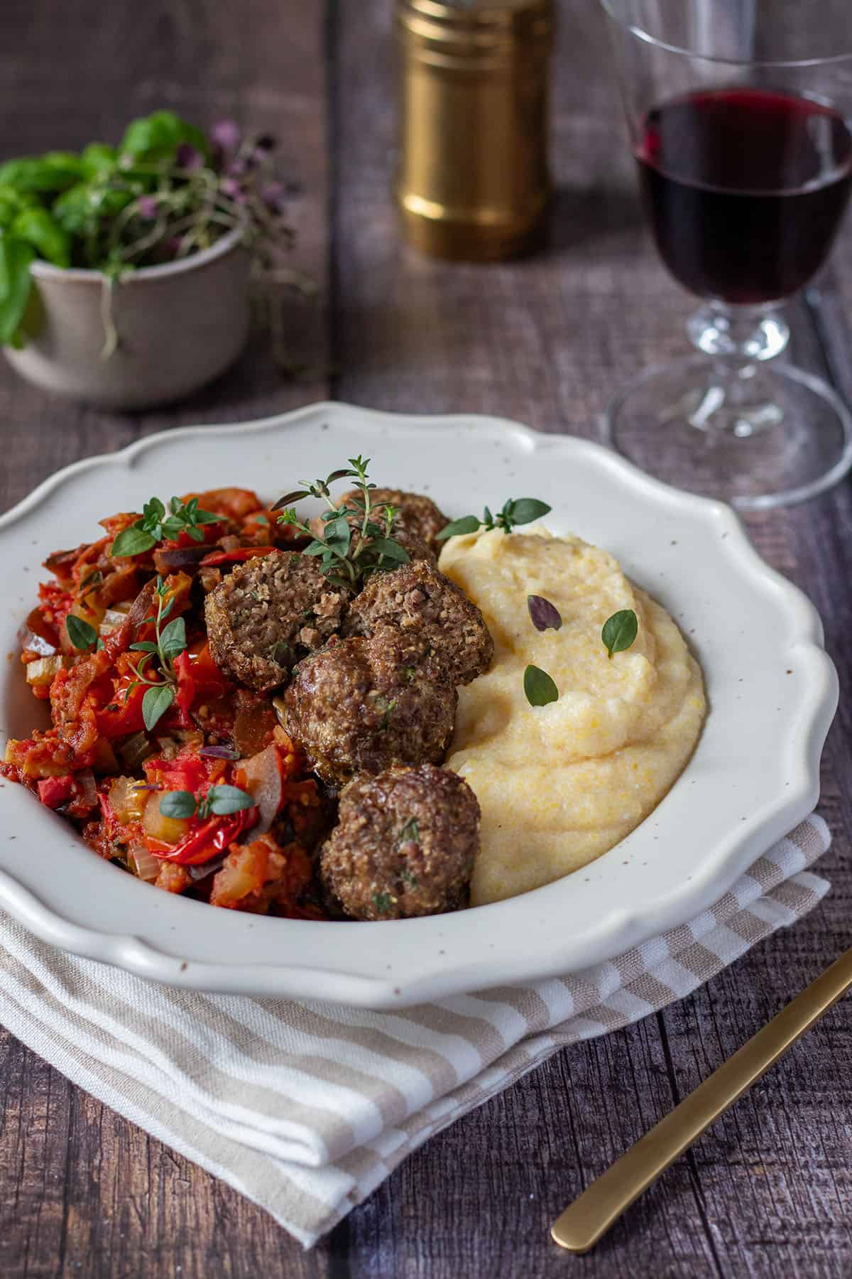 Ein Teller mit Polenta, Gem&uuml;se und Fleischb&auml;llchen, Deko im Hintergrund.
