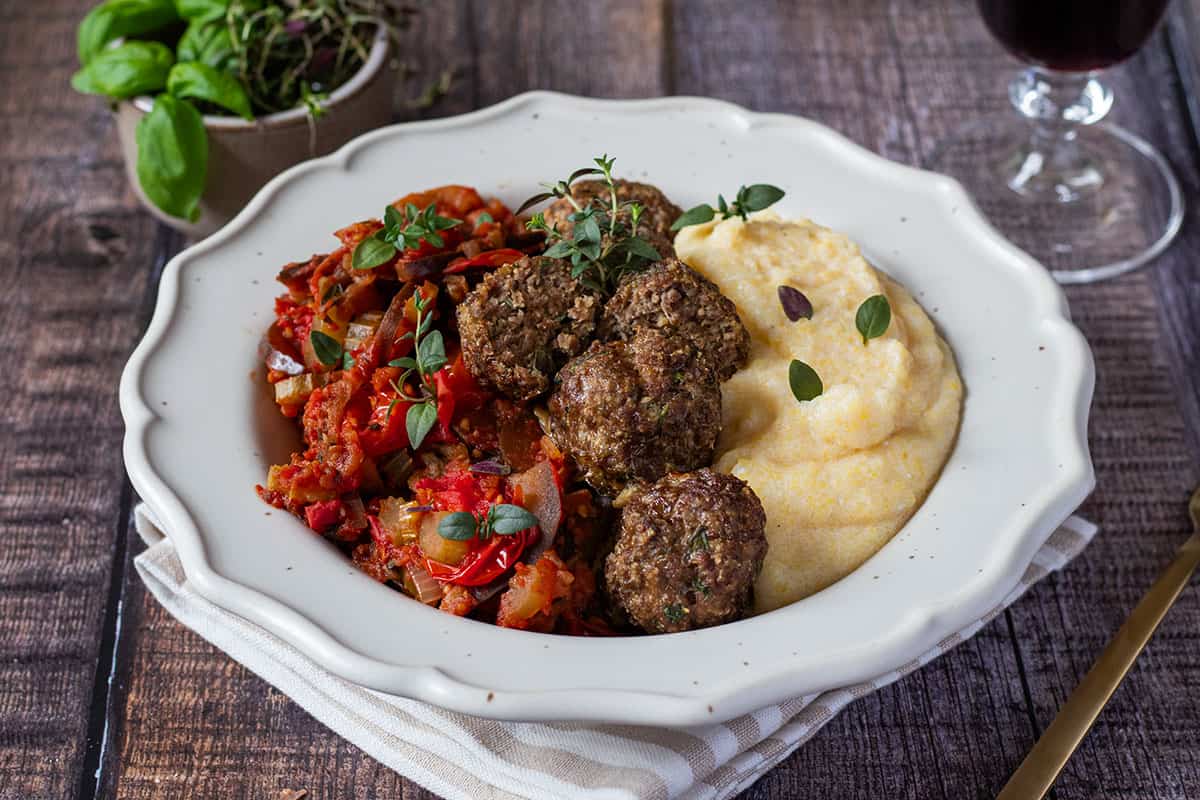 Italienische Polenta als Hauptgang serviert mit Gem&uuml;se und Fleischb&auml;llchen, Deko im Hintergrund.