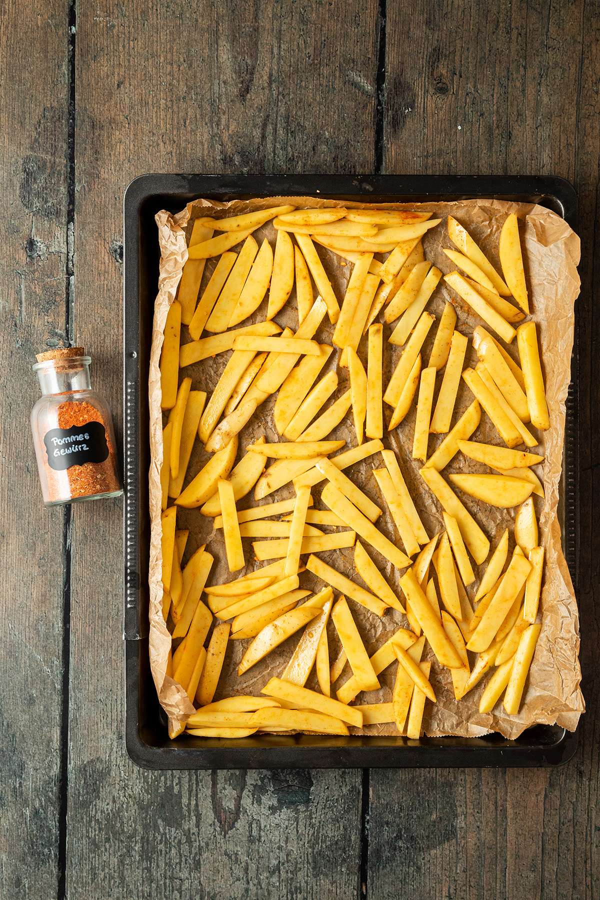 Ein Blech mit in d&uuml;nne Streifen geschnittene Pommes, daneben ein Gef&auml;&szlig; mit selbstgemachtem Pommes Gew&uuml;rz.