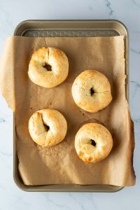 Vier goldbraune Protein Bagel auf einem Blech mit Backpapier.