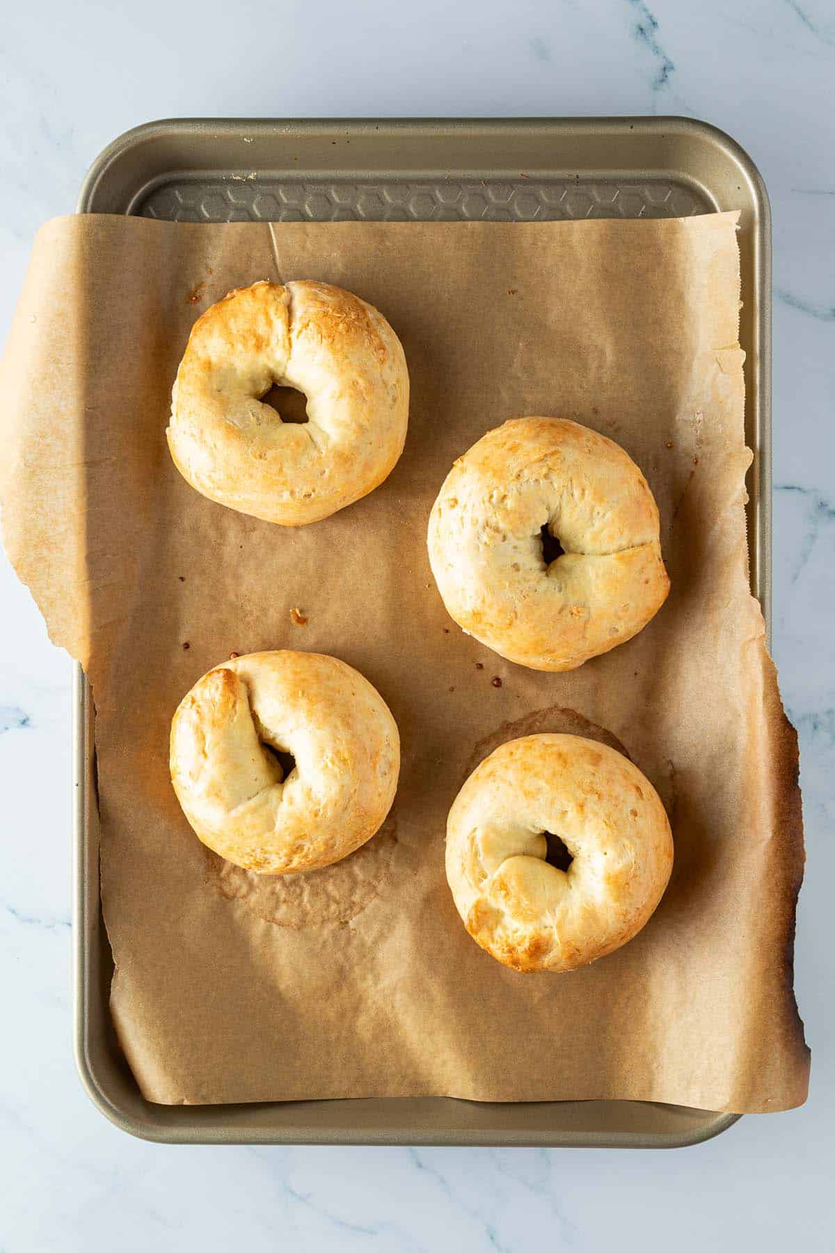 Vier goldbraune Protein Bagel auf einem Blech mit Backpapier.