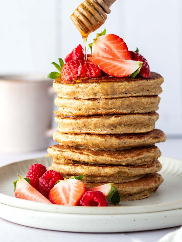 Auf einen Stapel aus Pancakes mit frischen Beeren wird Honig getr&auml;ufelt.