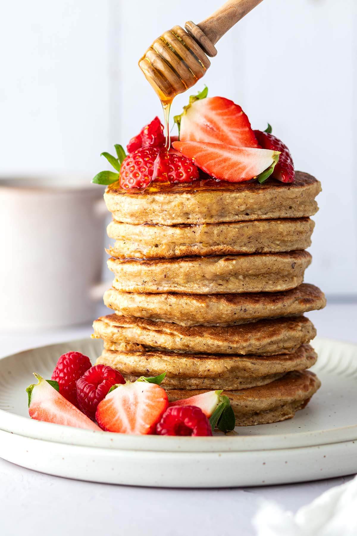 Auf einen Stapel aus Pancakes mit frischen Beeren wird Honig getr&auml;ufelt.