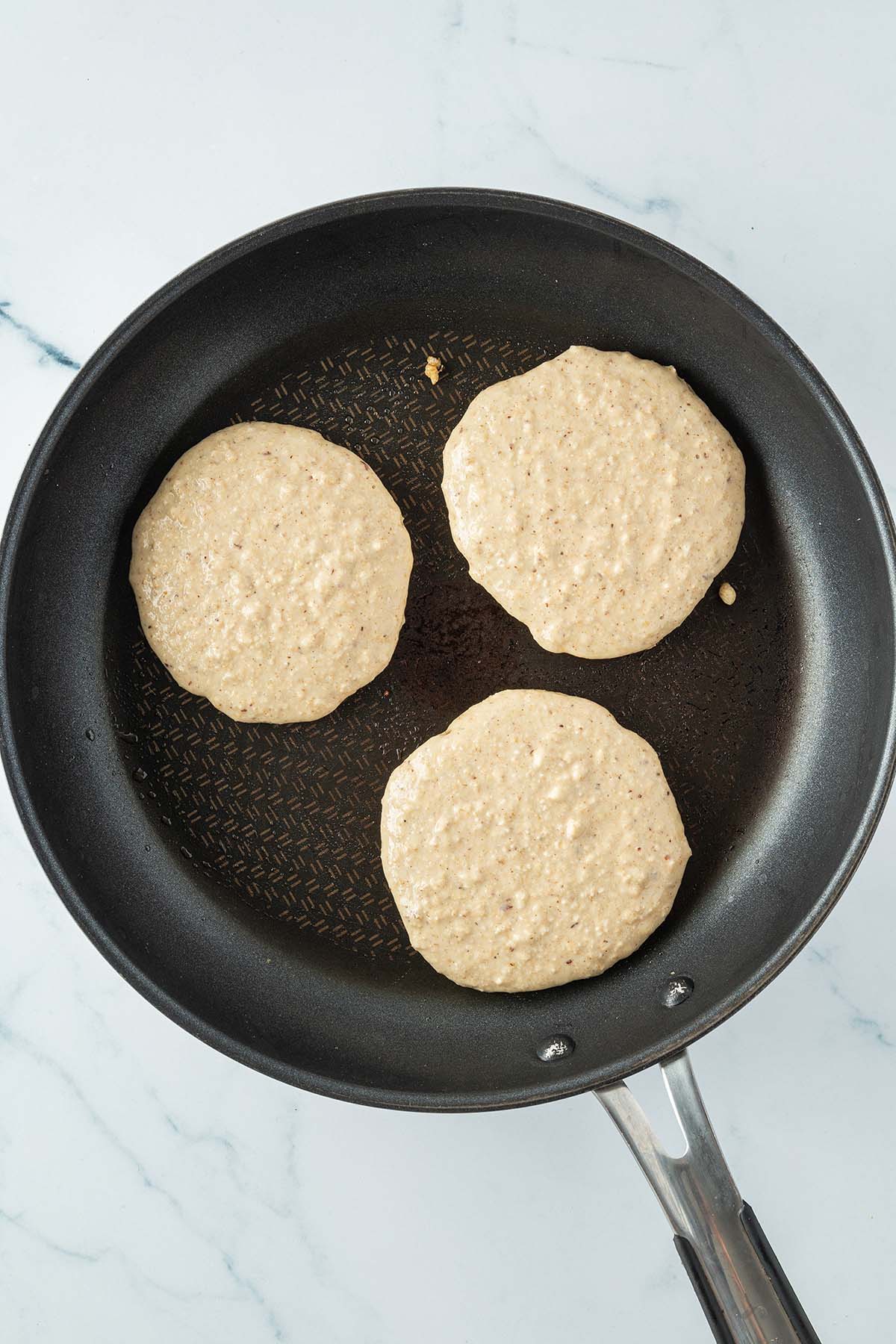 Drei Pancakes in einer Pfanne vorm Wenden.