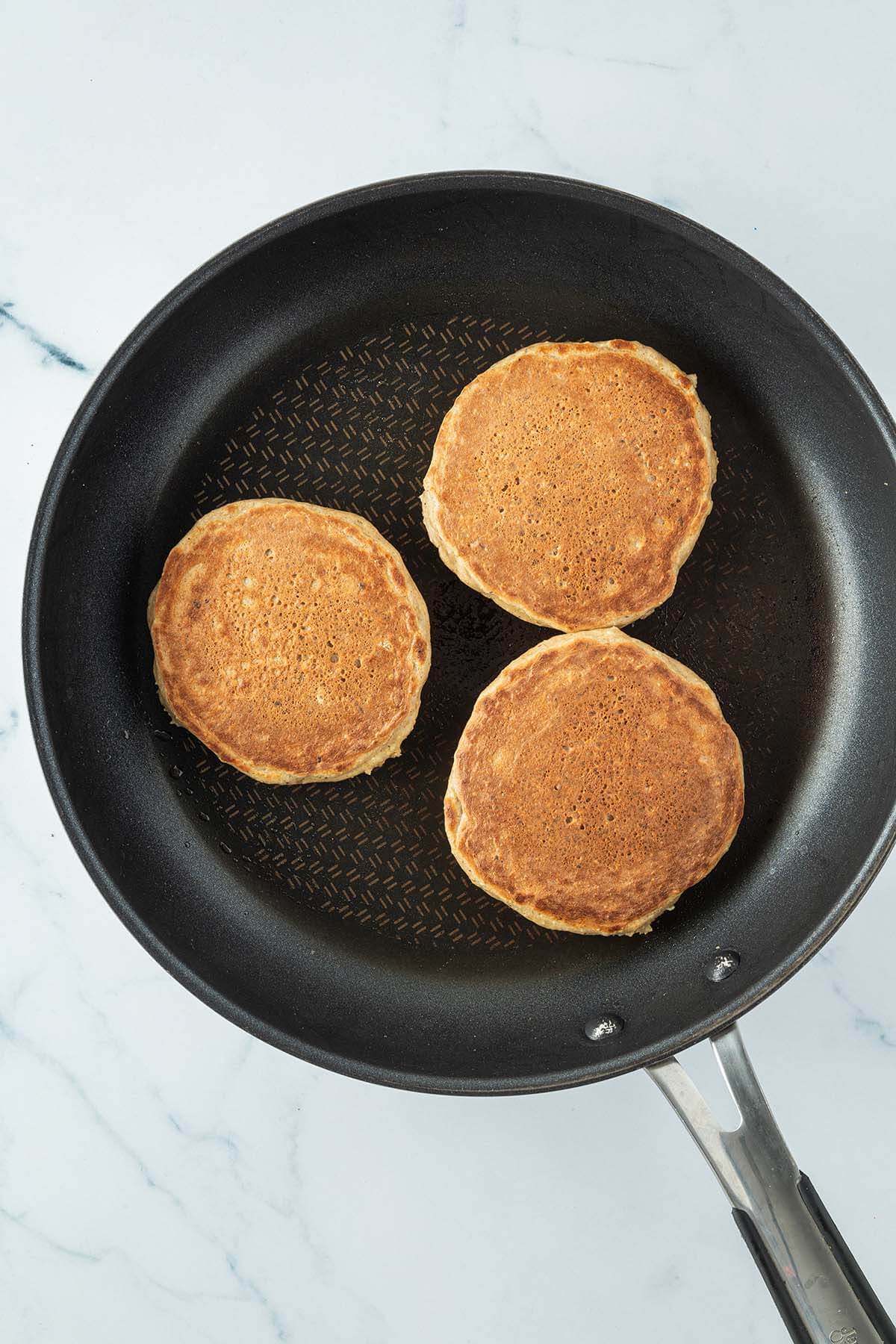 Drei goldbraune Pancakes in einer Pfanne.