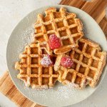 Drei dicke, fluffig Waffeln auf einem Teller, der auf einem Holzbrett steht.
