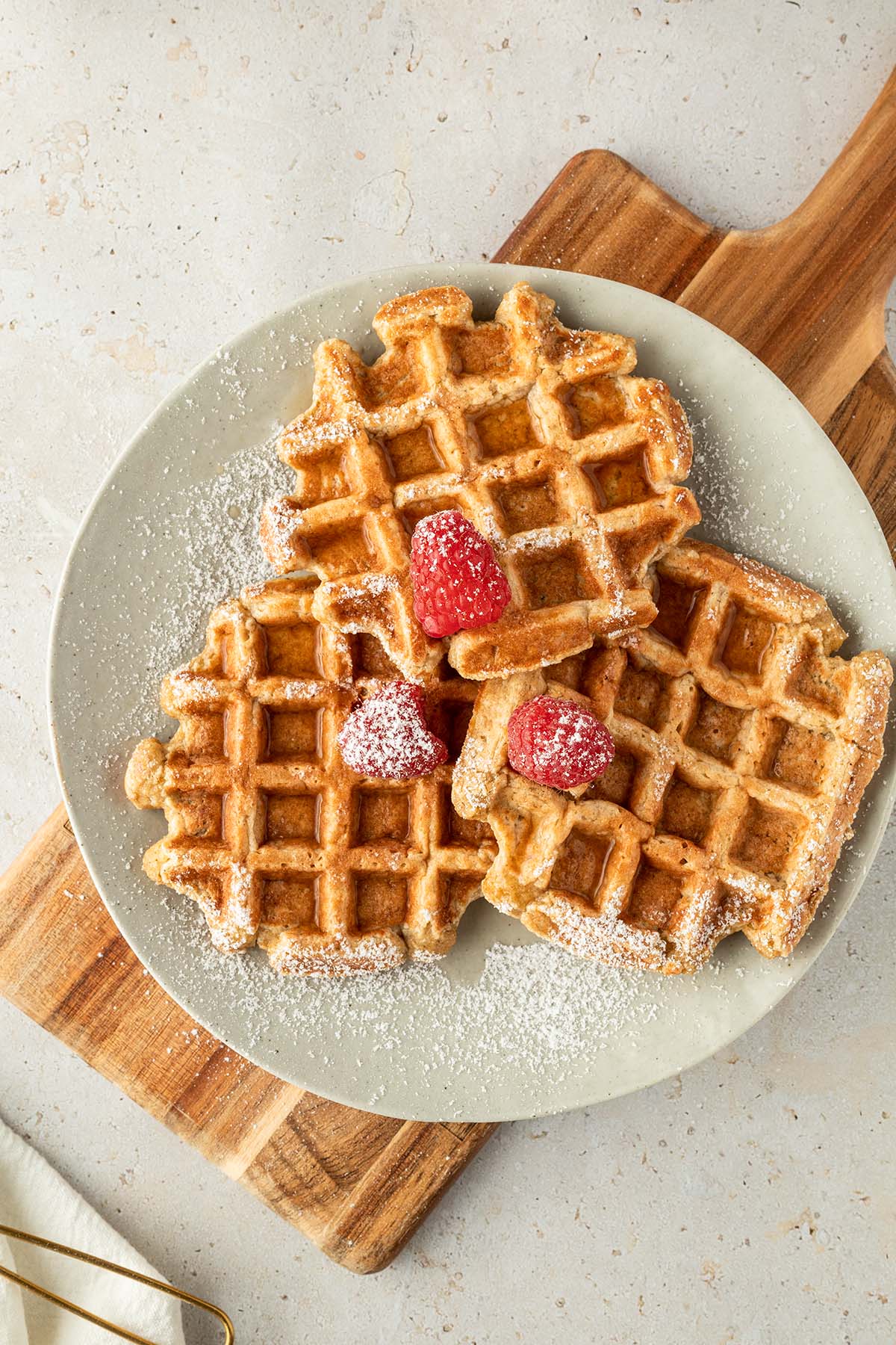Drei dicke, fluffig Waffeln auf einem Teller mit Himbeeren, Puderzucker und Sirup.