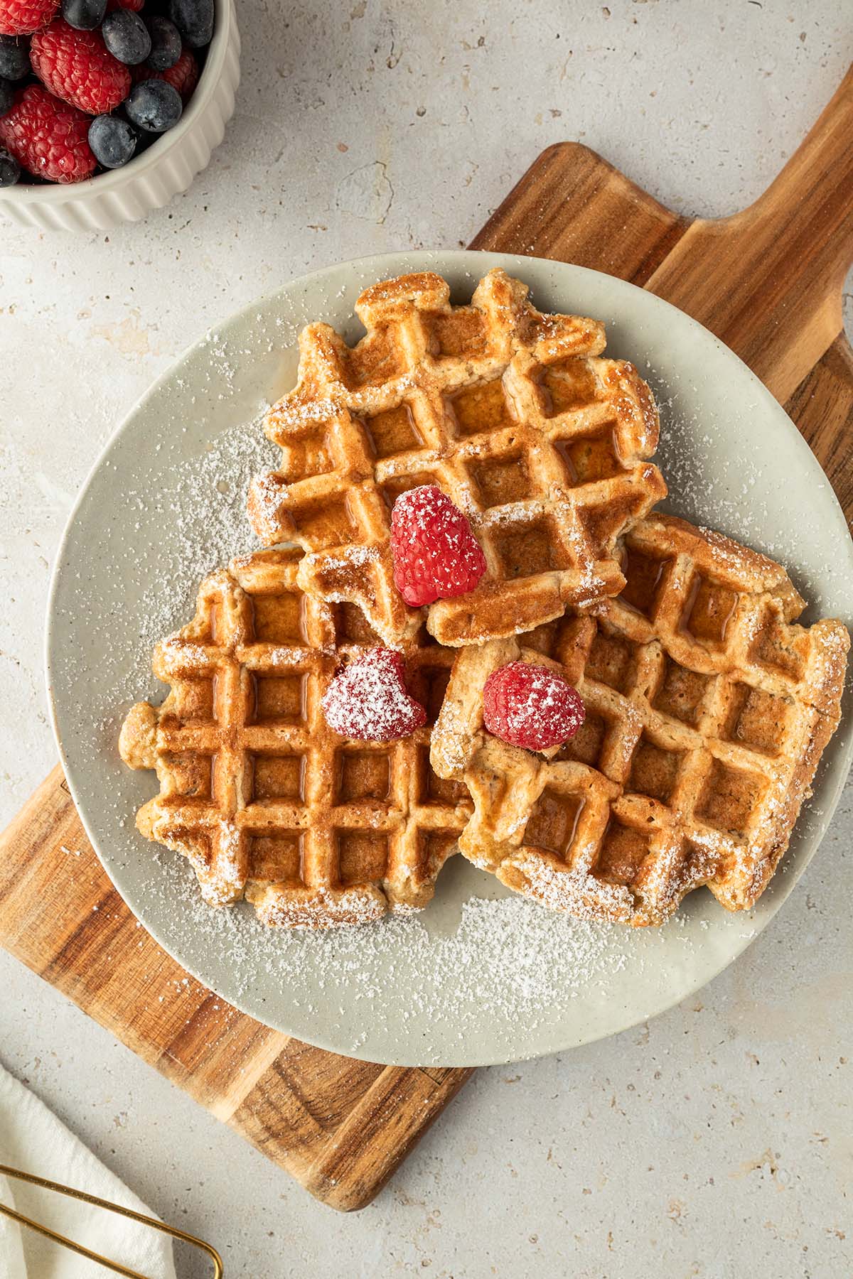 Drei dicke, fluffig Waffeln auf einem Teller mit Puderzucker, Beeren und Sirup serviert.