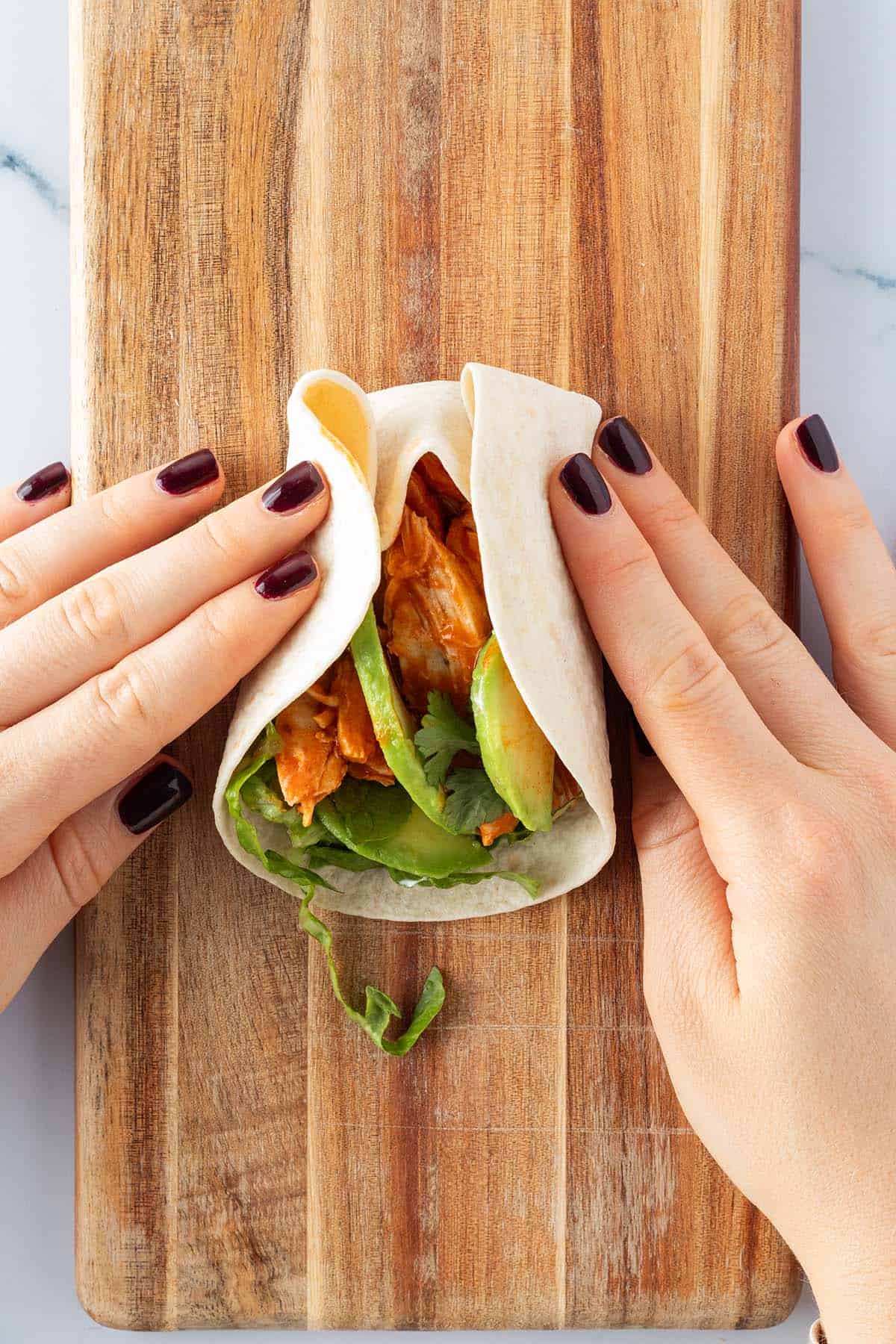 Nachdem das obere Ende von einem gef&uuml;llten Taco auf die F&uuml;llung gefaltet wurde, wurden die Seiten des Tortillas hochgeschlagen.