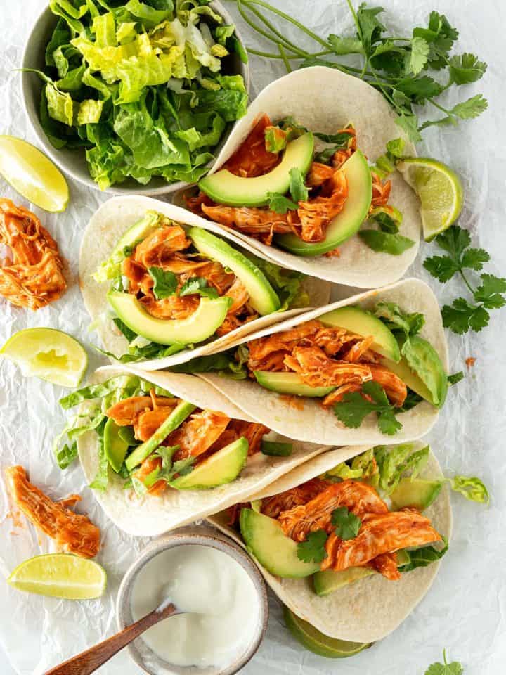 F&uuml;nf Tacos mit Pulled Chicken, Avocado und Salat auf einem wei&szlig;en Untergrund mit frischen Kr&auml;utern, Salat und saurer Sahne.