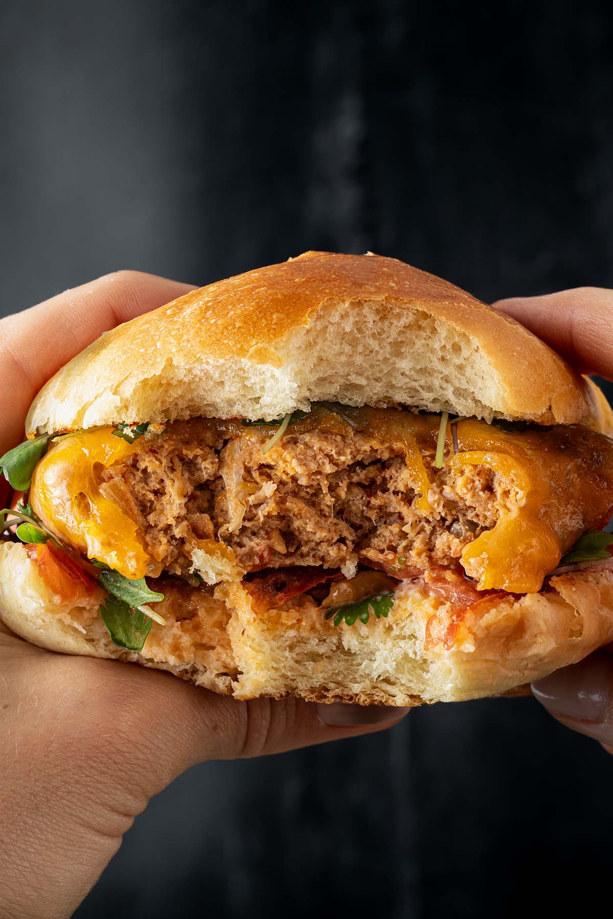 Nahaufnahme von einem angebissenen Puten Burger, den jemand in der Hand h&auml;lt vor einem dunklen Hintergrund.