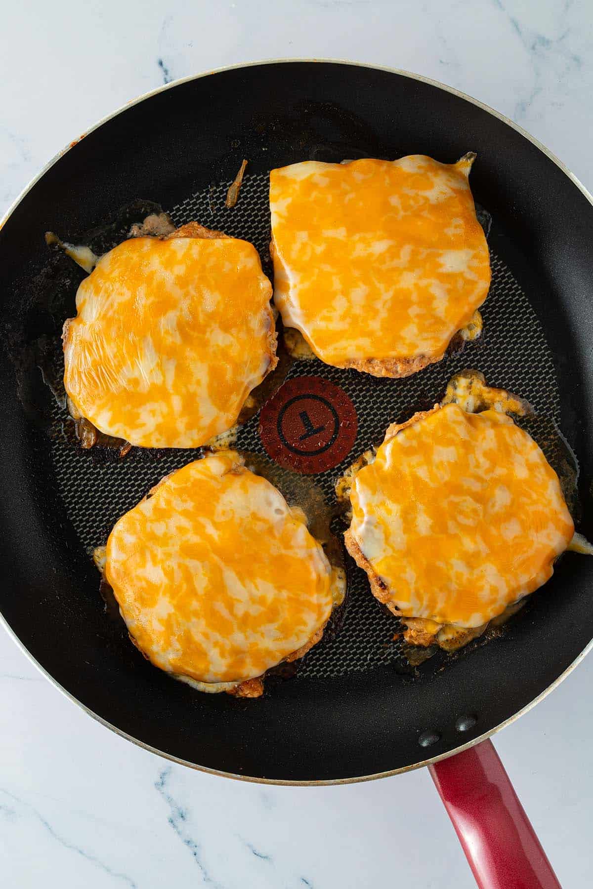 Vier Puten Patties werden in einer Pfanne mit K&auml;se &uuml;berbacken.