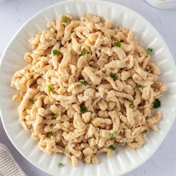 Vogelperspektive auf einen Teller mit Quarksp&auml;tzle mit frischer Petersilie und Deko im Bildrand.
