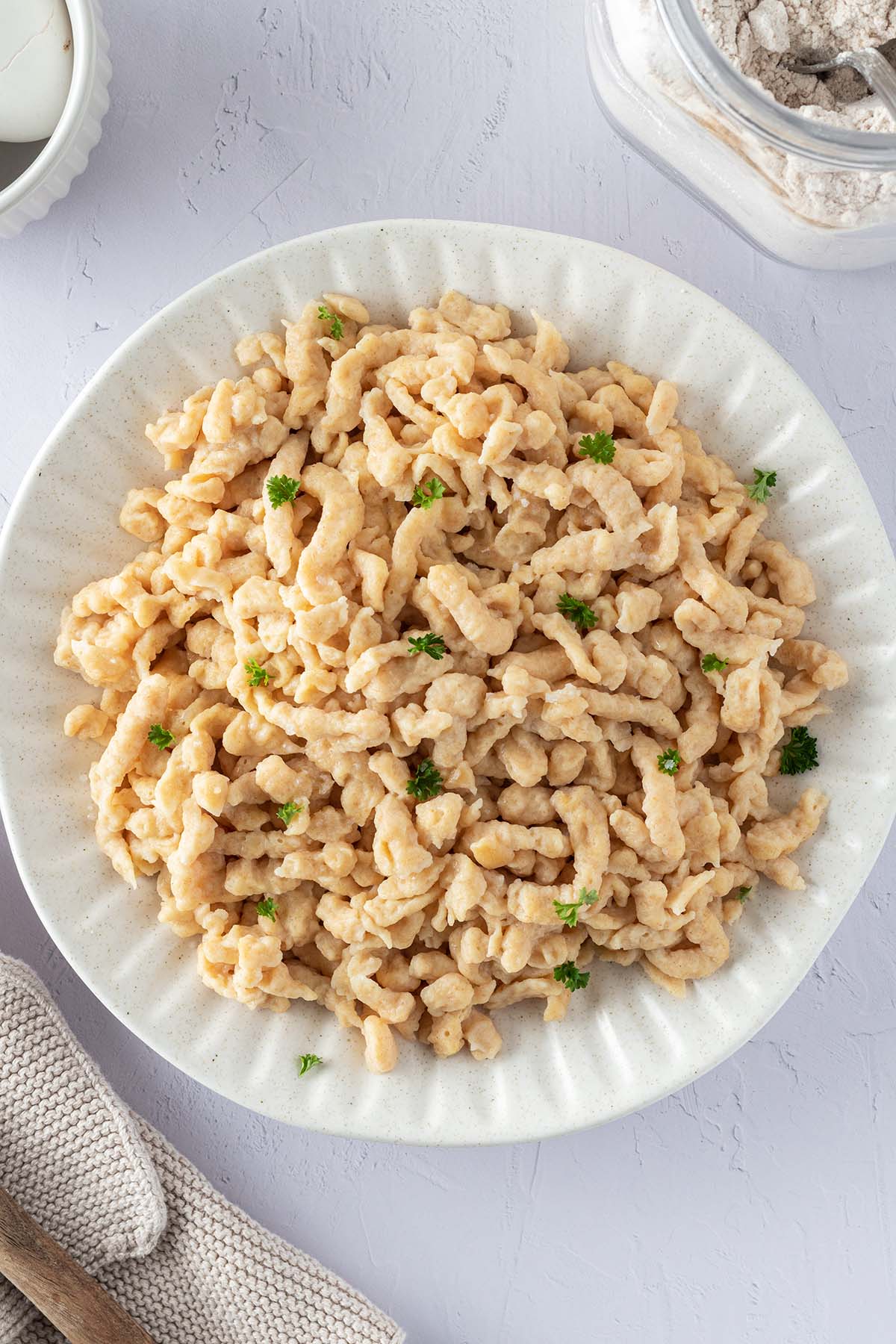 Vogelperspektive auf einen Teller mit Quarksp&auml;tzle mit frischer Petersilie und Deko im Bildrand.