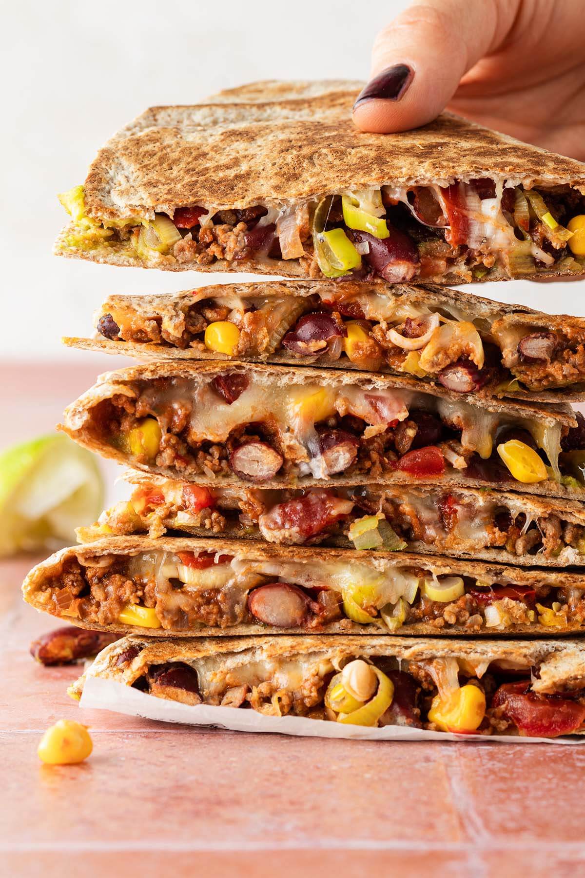 Ein Stapel Quesadilla mit Hackfleisch, wo eine Hand einen Quesadilla wegnimmt.