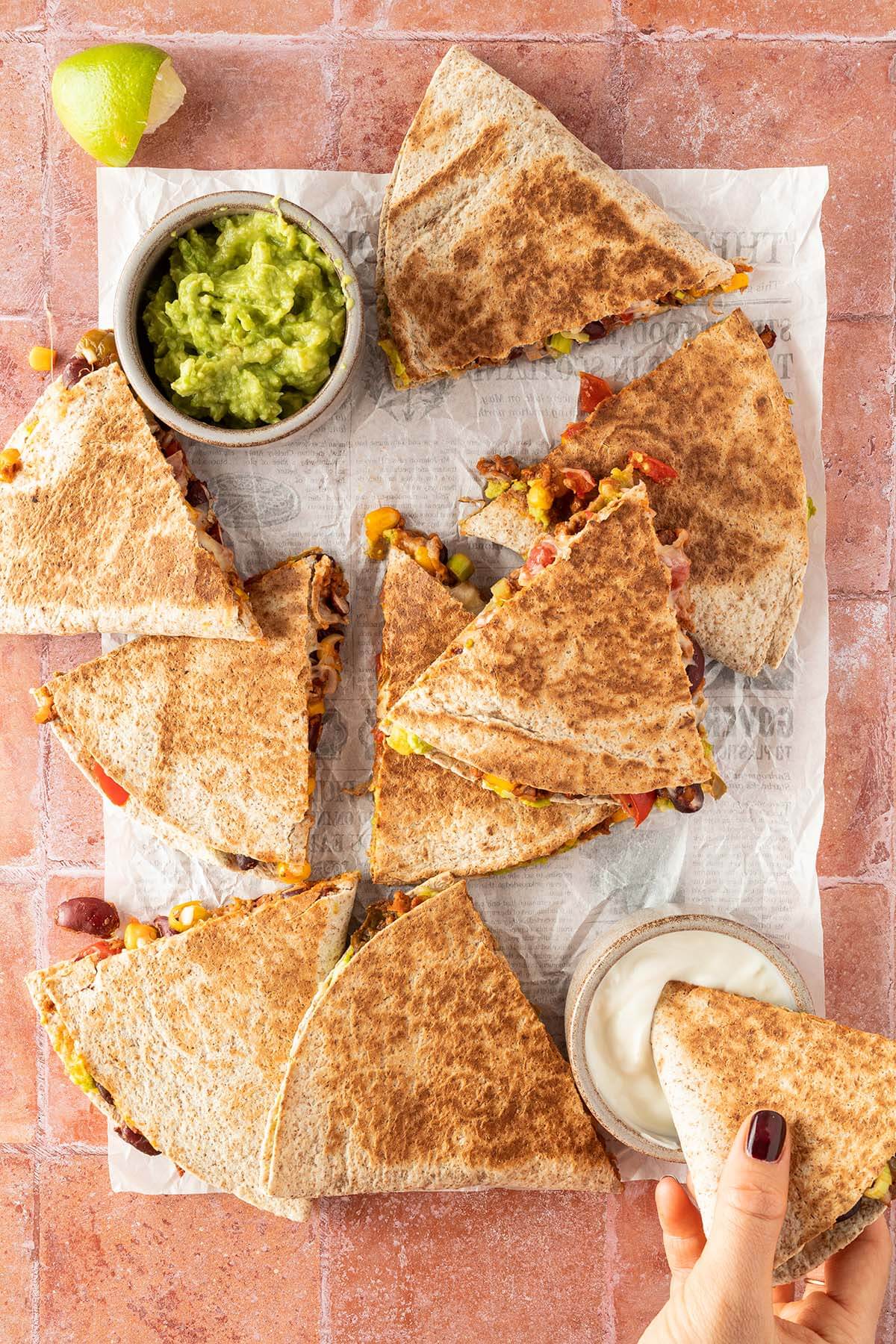 Vogelperspektive auf in Dreiecke geschnittene Quesadilla auf roten Flie&szlig;en mit zwei Dip-Sch&uuml;sseln.