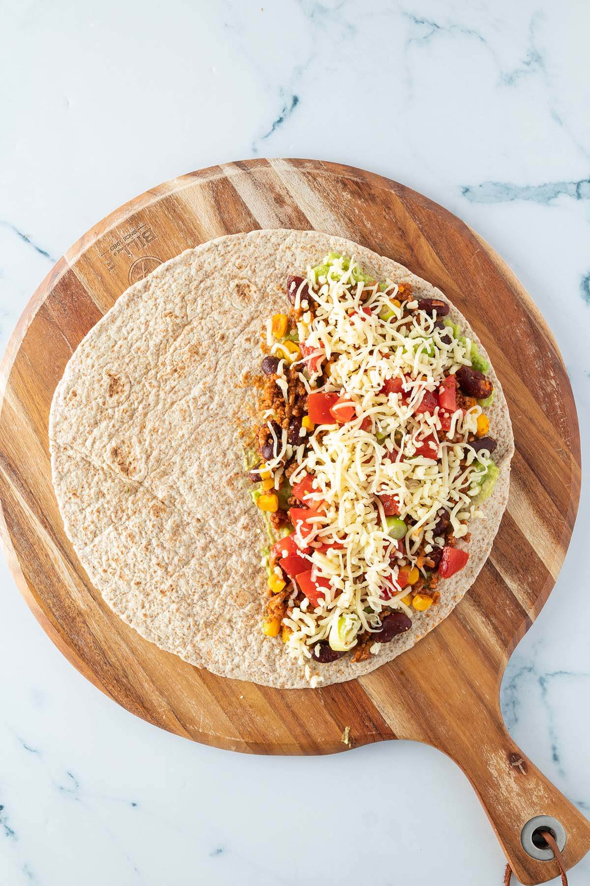 Ein zur H&auml;lfte belegter Tortilla-Wrap auf einem runden Holzbrett.