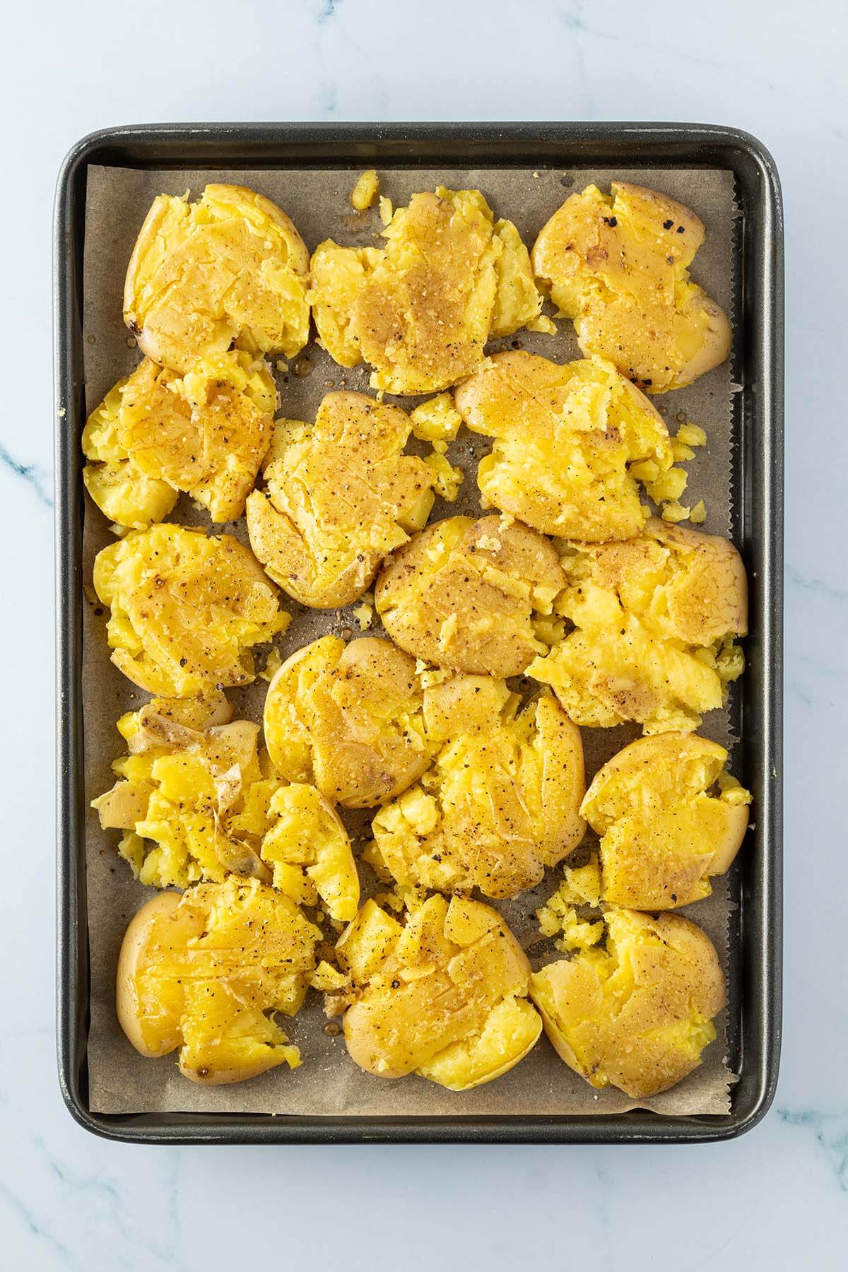 Zerdr&uuml;ckte und mit &Ouml;l marinierte Kartoffeln auf einem Blech.