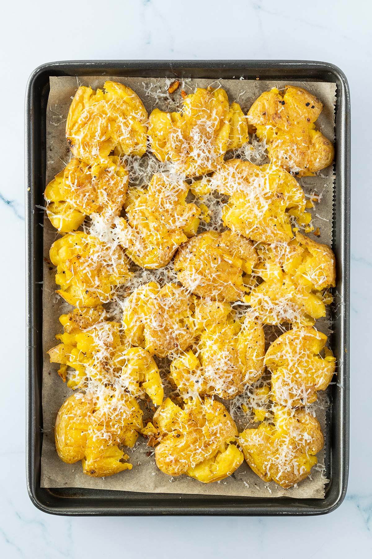 Quetschkartoffeln auf einem Blech mit frisch geriebenem Parmesan.