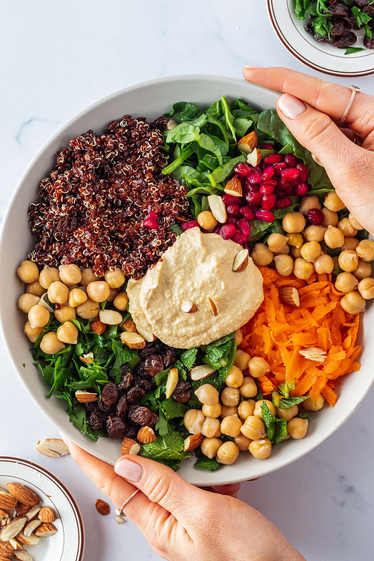 Zwei Hände halten einen Teller, wo die einzelne Komponenten eines Quinoa Salats nebeneinander angerichtet sind.