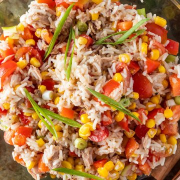 Nahaufnahme von einer Sch&uuml;ssel Reissalat mit Thunfisch, Tomaten, Mais, Paprika und Fr&uuml;hlingszwiebeln.