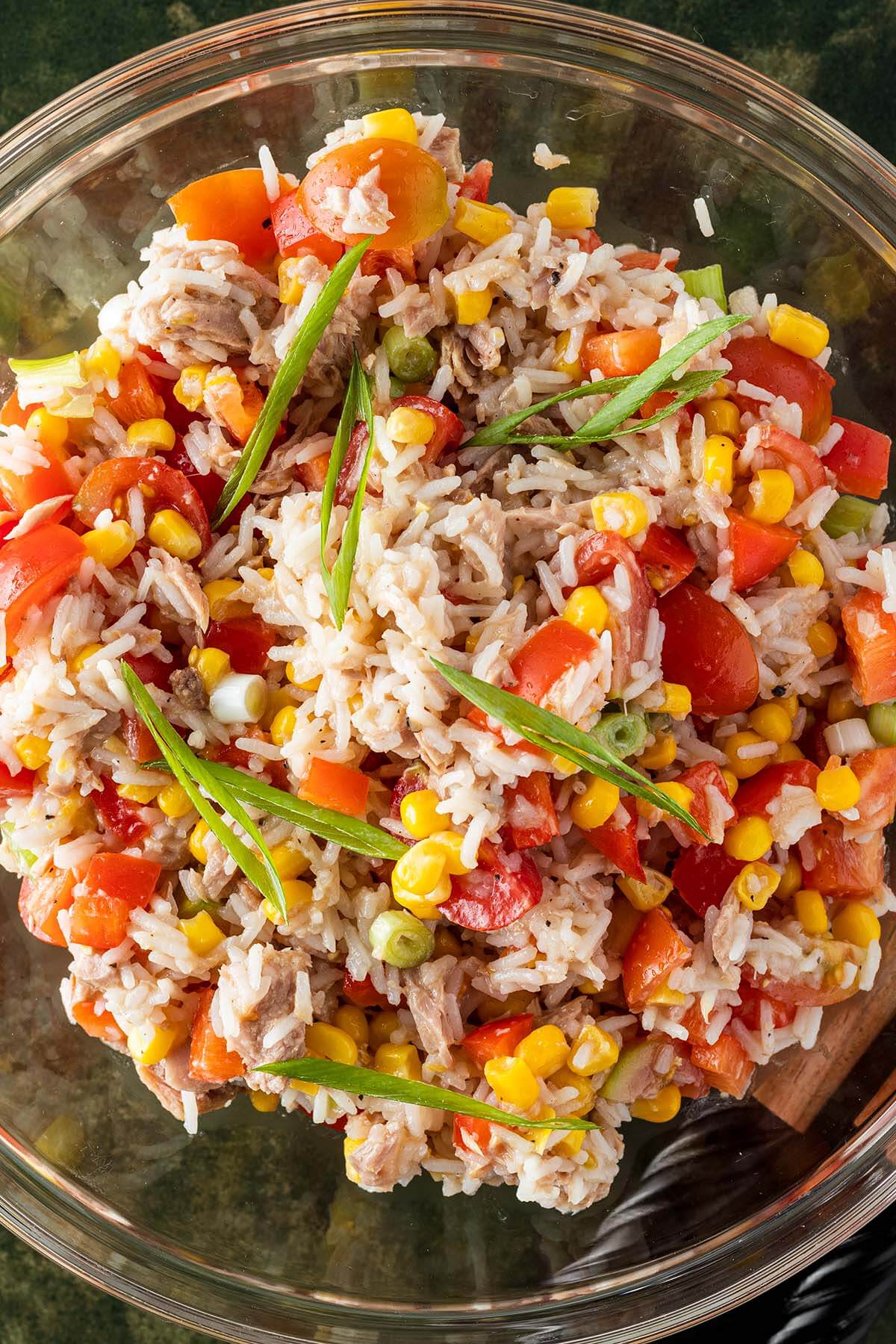 Nahaufnahme von einer Sch&uuml;ssel Reissalat mit Thunfisch, Tomaten, Mais, Paprika und Fr&uuml;hlingszwiebeln.