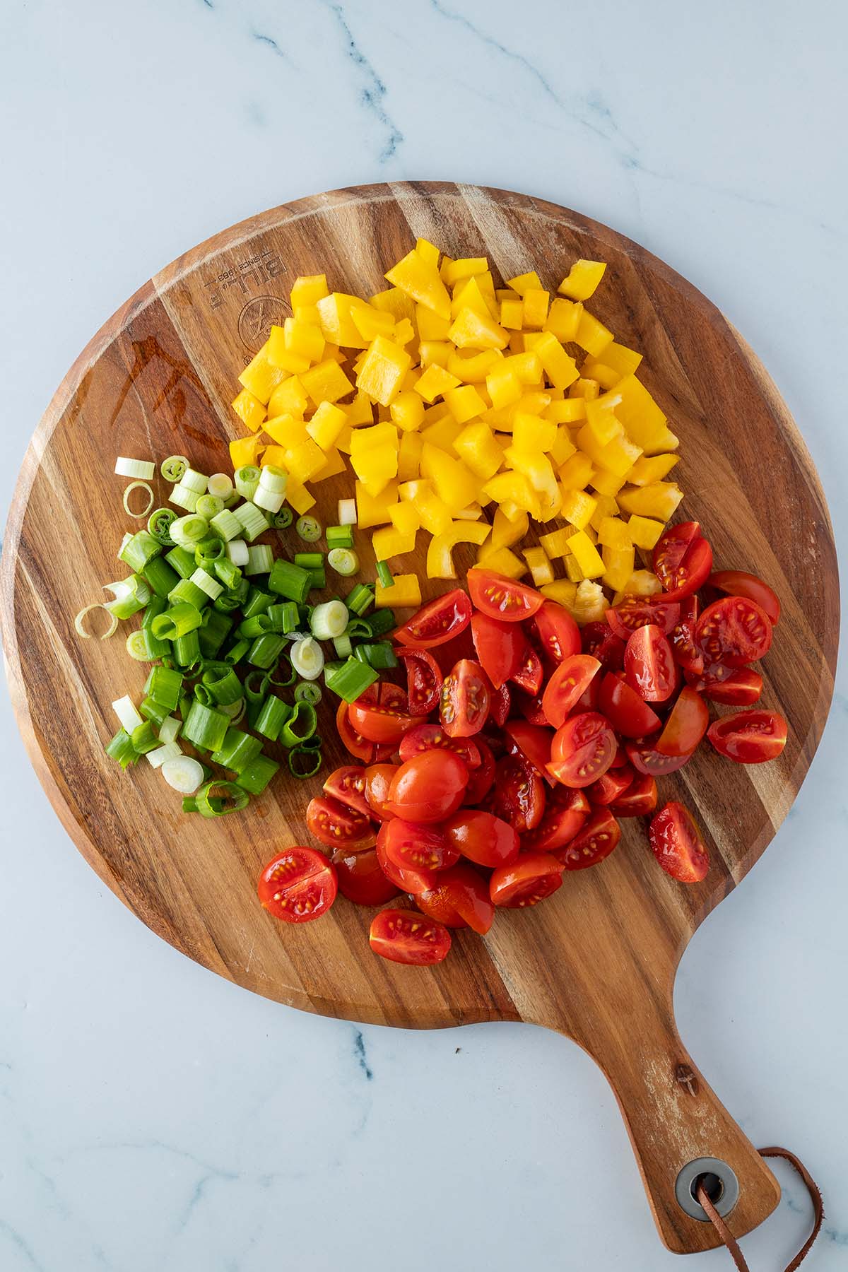 Kleingeschnittene Paprika, Kirschtomaten und Fr&uuml;hlingszwiebeln auf einem Holzbrett.