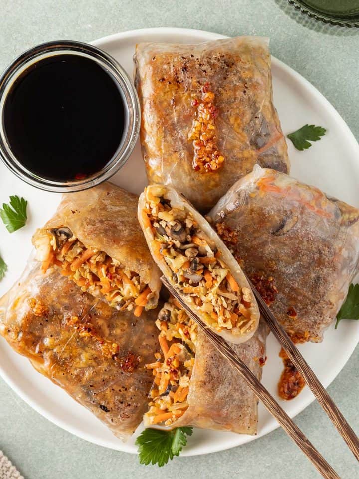 Reispapier Dumplings auf einem Teller mit Sojasauce, eine H&auml;lfte wird von St&auml;bchen gehalten.