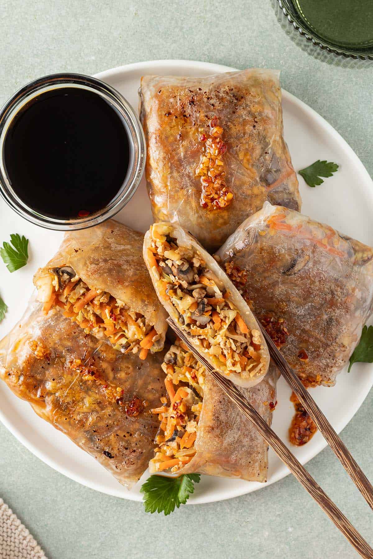Reispapier Dumplings auf einem Teller mit Sojasauce, eine H&auml;lfte wird von St&auml;bchen gehalten.