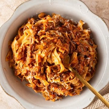 Selbstgemachte Bandnudeln mit italienischem Rinderragout und frisch geriebenem Parmesan in einem tiefen Teller.
