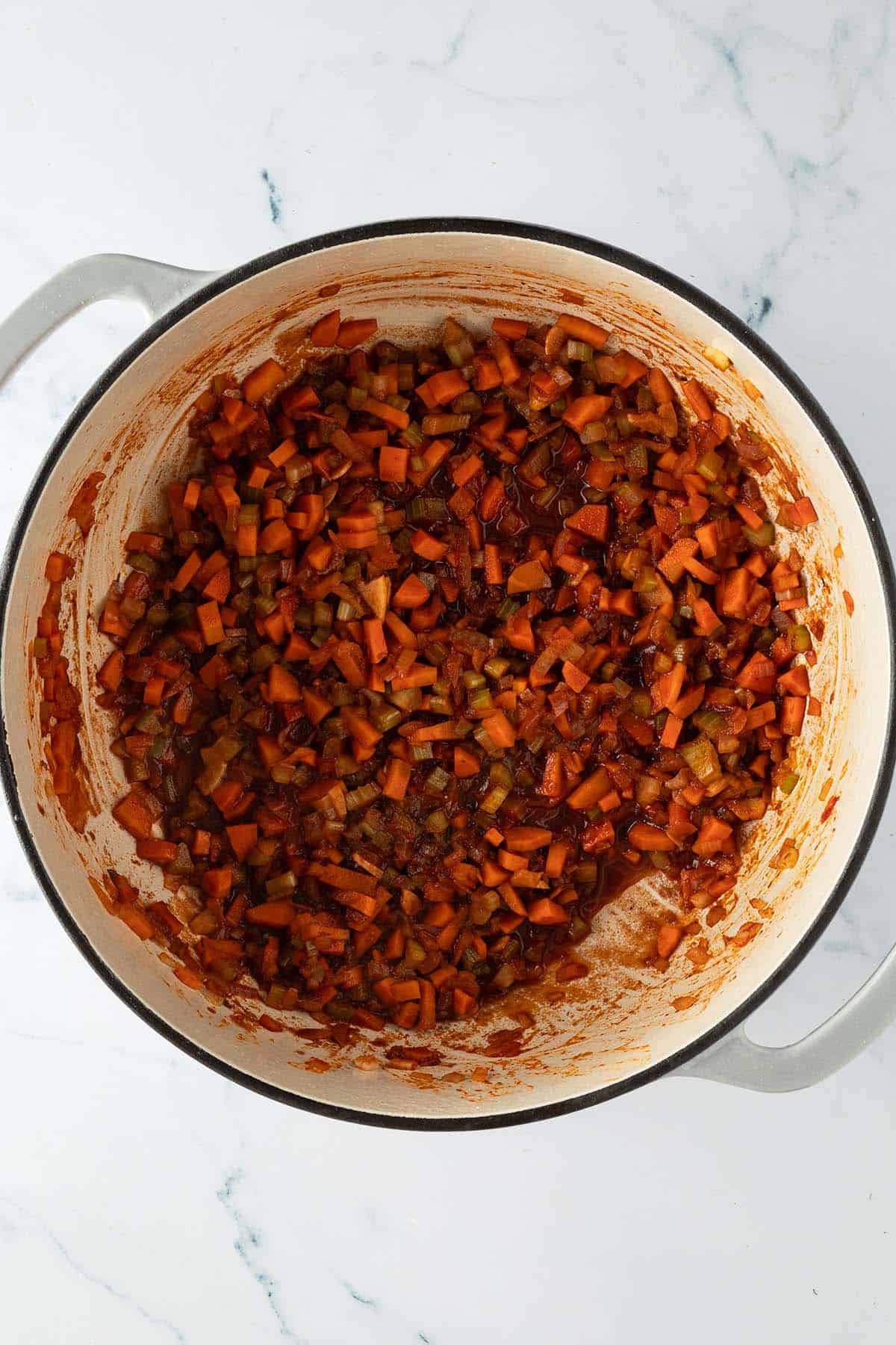 Angebratenes Gem&uuml;se mit Tomatenmark in einem Topf mit verkochten Rotwein.