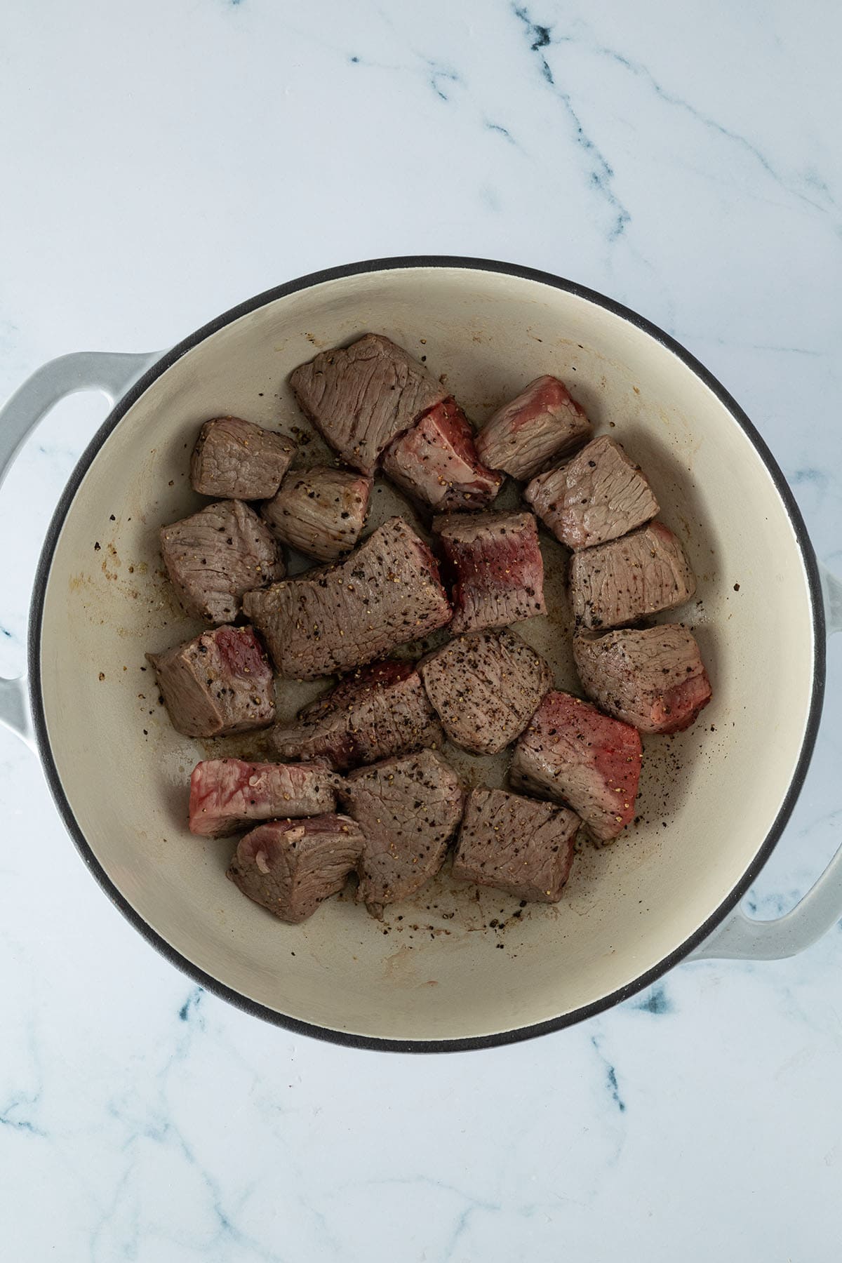 In W&uuml;rfel geschnittenes Rindergulasch wird in einem Gusseisentopf rundum angebraten.